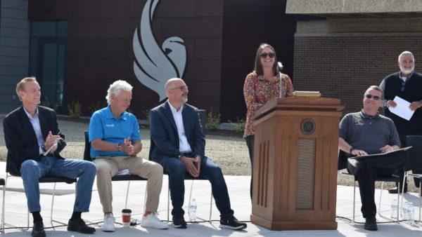 MaryBeth Stopoulos standing at podium outside Building 3 with 4 people seated by podium