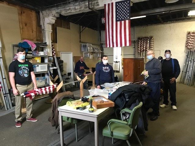 a group of masked men around a table with power tools and flags