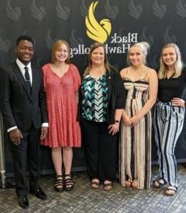 5 people standing in front of backdrop with college logo